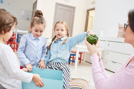 幼儿园学习者在课上指的是他们的老师手里放着青椒