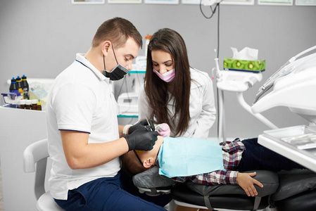 年轻的男性牙医在白色 t恤与一名女助手帮助他是给孩子牙科治疗在现代牙科诊所