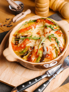 烤茄子, 西葫芦和西红柿, 奶酪和新鲜的芝麻菜, 用叉子和小刀在木砧板上的陶瓷碗里。