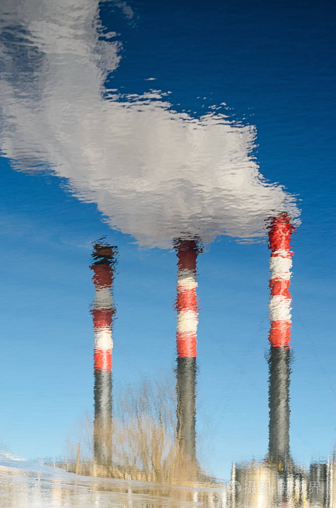 植物的烟烟囱反映在水中用烟雾对付清澈的蓝天的植物管道水面上反射