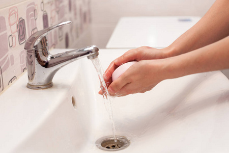 一个女人用肥皂在浴室的白色水槽里洗手。