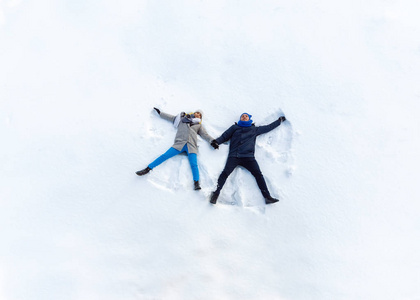 快乐的年轻夫妇在冬季公园躺在雪地上。做雪天使。顶部视图