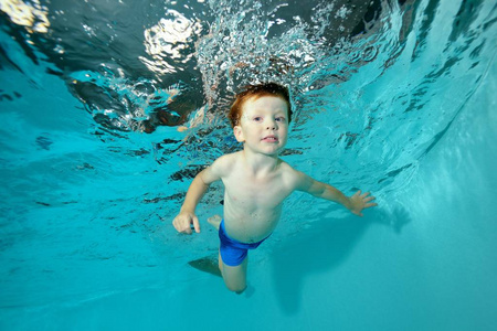 美丽的小男孩游泳水下池在蓝色背景。肖像。在水底下射击。水平视图