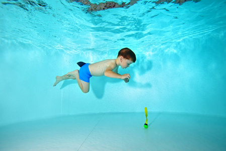 这个孩子在游泳池里从事水下运动。在水下游泳的蓝色背景和看底部。肖像。在水下射击。水平视图