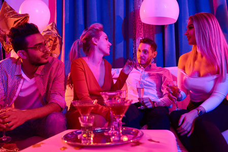 一群人在豪华的房子聚会上, 喝着酒精饮料, 在昏暗的蓝光照亮的房间里聊天