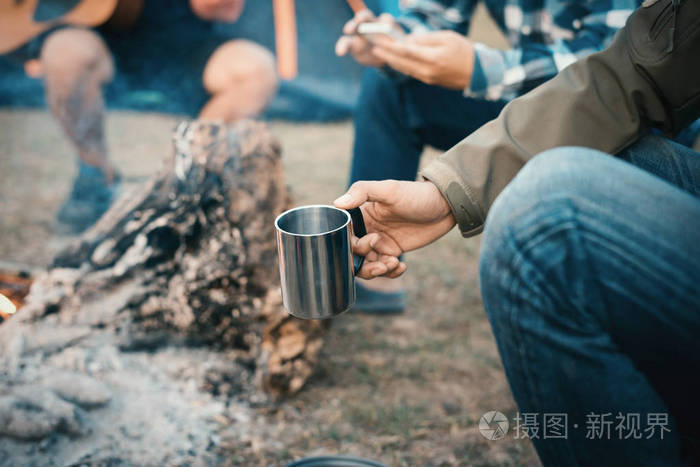 男人的旅行者手里捧着杯茶近火在户外，周五