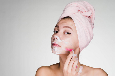 滑稽的年轻女孩用粉红色的毛巾在她的头上剃须她的脸像一个男人