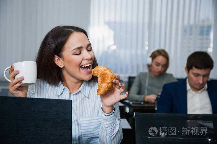 放松的女学生与杯茶或咖啡和小吃牛角面包和苹果一群人在背景上快乐的