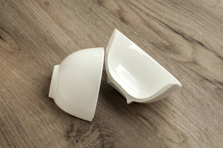 碎在二半小白色瓷碗特写在木板背景上照片
