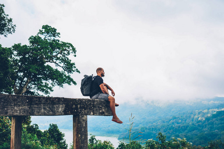 体贴的男性徒步旅行者与背包享受绿色山脉的环境美景和景观的观点。梦幻般的游客与旅行背包考虑下一次旅行探索亚洲自然