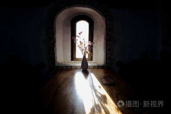 桌子上的一束花束在明亮的太阳一间漆黑的房间里, 阳光透过狭窄的窗户