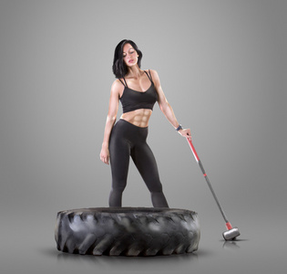 运动年轻女子健身锻炼用锤子和轮胎上灰色工作室背景
