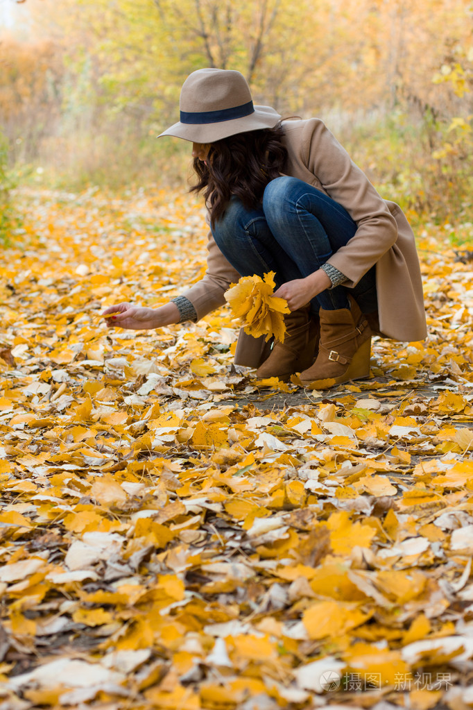 穿着大衣的女孩收集树叶在森林里