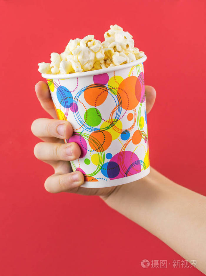 儿童手用五颜六色的玻璃爆米花在红色背景