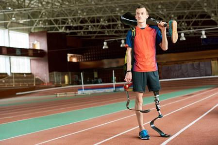 年轻截肢运动员的全长画像站立在现代室内体育场持有备用假肢腿
