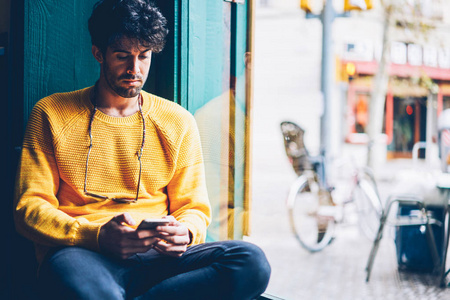 穿着黄色毛衣的长胡子英俊的年轻人阅读在智能 coworking 空间中连接到4g 互联网上的手机接入通知