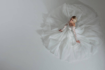 美丽的新娘，在奢华的婚礼礼服，裙子躺在附近，一个圆的形状。白色背景，顶视图
