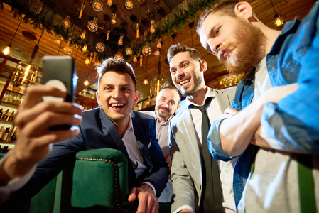 微笑胡子的朋友采取自拍在智能手机的帮助下, 而期待已久的聚会在现代酒吧