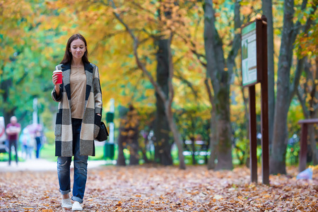 快乐美丽的女人，在下秋天的落叶的秋天公园里喝咖啡