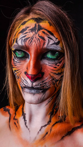 在黑暗的背景下, 一只老虎被画成一张脸的女孩