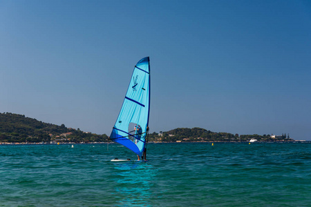 男人们在科西嘉蔚蓝的海面上冲浪。蓝色风冲浪在前景, 科西嘉自然在背景