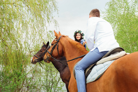 马男一位女友坐在马背上, 对着坐在马背上看着她的男友微笑照片