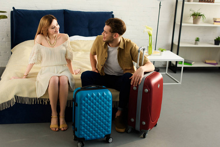 愉快的夫妇与手提箱准备假期坐在床上