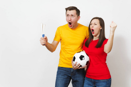 有趣的疯狂欢快的年轻夫妇, 妇女, 男子, 足球球迷在黄色和红色制服振作起来支持队与钢管足球隔离在白色背景。体育, 家庭休闲, 