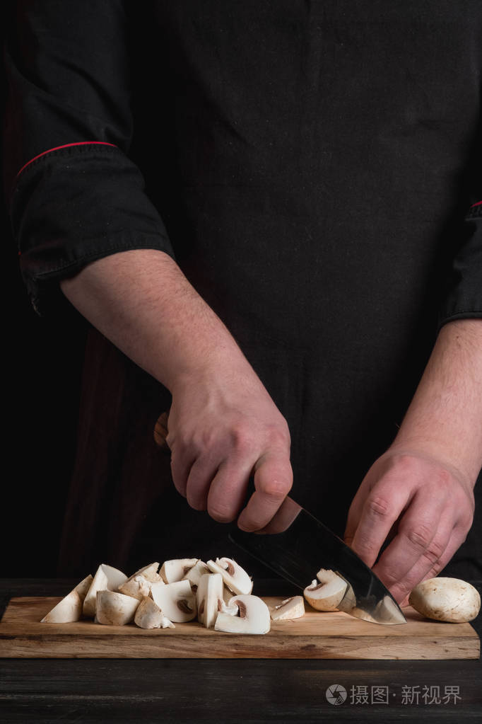 餐桌背景下男厨师手抓刀和切白食用菌的特写