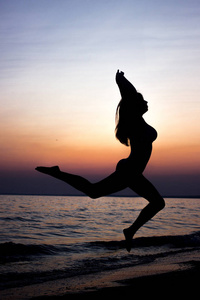 女人在日落在海边的沙滩上跳跃。自由生活的概念