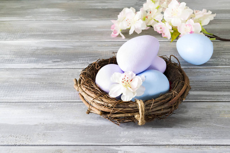 手绘复活节彩蛋在一个巢与春天的花朵在一个木灰色的背景。复活节快乐
