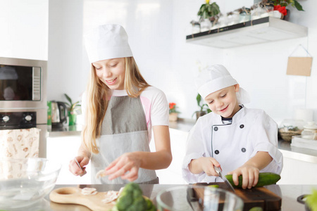 一个哥哥和一个姐姐在现代化的厨房里切蔬菜。快乐家庭烹饪理念
