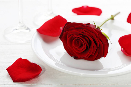木桌上白盘子里的红玫瑰