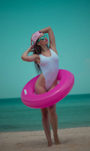 美丽快乐的年轻女子泳装, 帽子和太阳镜与粉红色充气环有乐趣, 享受阳光明媚的夏日在她的海滩热带假日