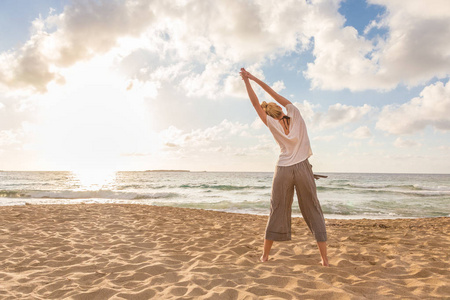 女人上练瑜伽的海滩在日落时分