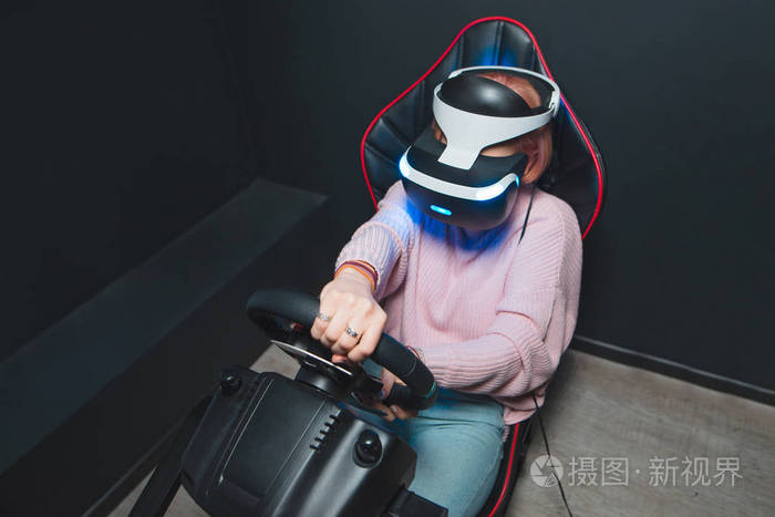 一个年轻的女孩玩一个虚拟现实的耳机在汽车模拟器的头上的 Vr 比赛。虚拟现实的概念。现实游戏