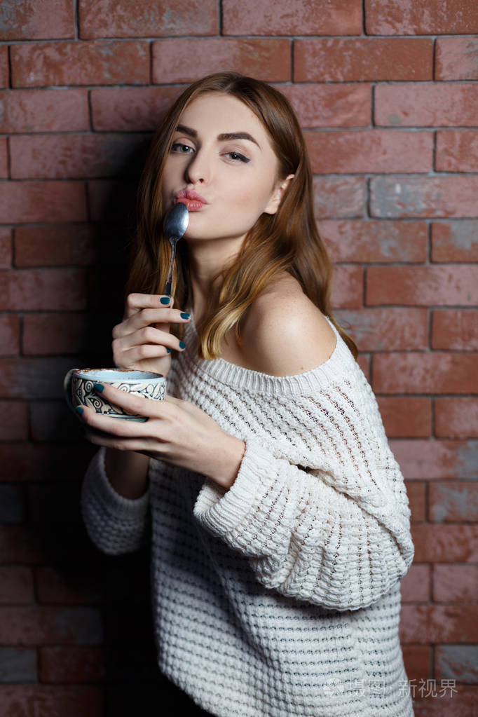 年轻漂亮的女人在咖啡馆里喝着一杯咖啡, 上面挂着红砖墙的背景