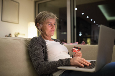高级女人坐在沙发上，在线购物的笔记本电脑