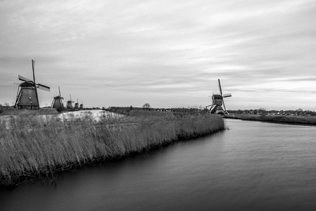 黑色白色风车和水运河上在荷兰风车村，日落的照片