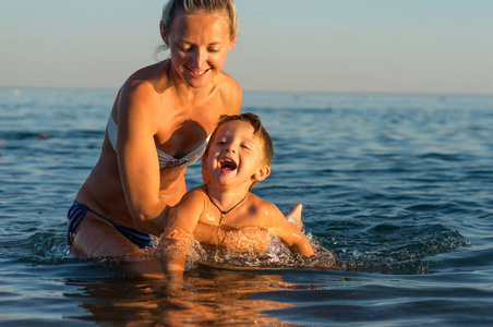 年轻的母亲和微笑宝贝男孩儿子在沙滩上玩了一天时间。积极的人类情感，感情快乐