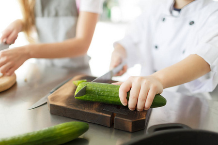 小男孩与女性切开新鲜的黄瓜在木板, 烹调在厨房里。健康食品的概念
