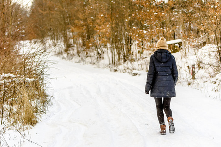 穿着冬衣走路的女孩。森林里雪路上的女人