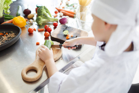 小男孩在木板上切新鲜的黄瓜, 在厨房里做饭。健康食品的概念