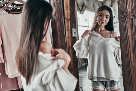 亚洲年轻女子穿着白色上衣, 站在镜子前的家里