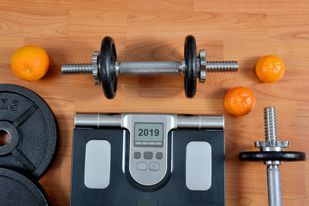 黑色哑铃与金属圆盘和体重秤在健身房。2019新年健康解决方案