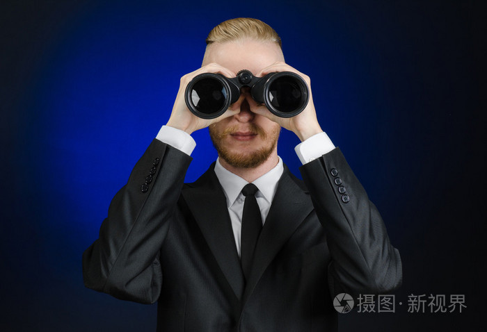 商业和搜索主题: 穿着黑色西装的男子手拿着黑色双筒望远镜在深蓝色