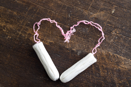 两个干净的白色卫生棉，形状在心脏上，躺在木制的SUR上