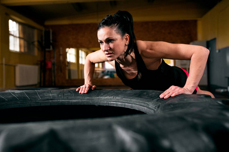 激烈的 crossfit 锻炼在黑暗的健身房, 紧张的年轻运动妇女做俯卧撑轮胎