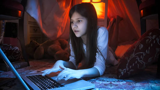晚上躺在地板上的可爱女孩的肖像和使用笔记本电脑