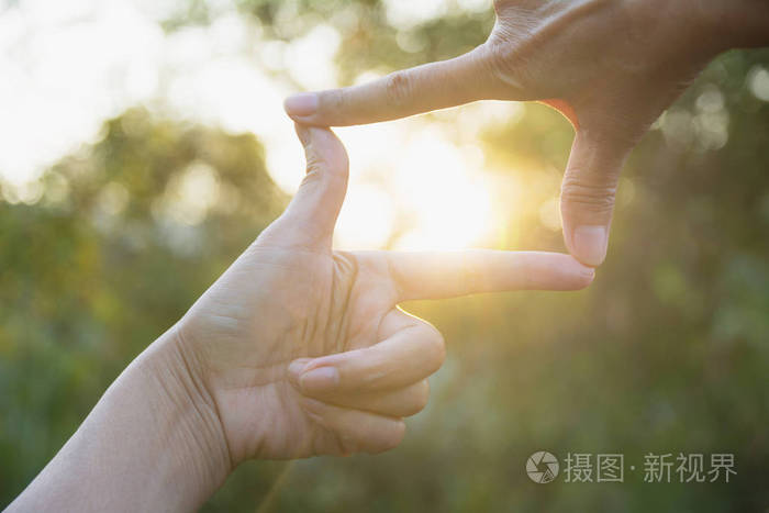 双手做框架手势的闭合。关闭女人的手做框架手势与日落